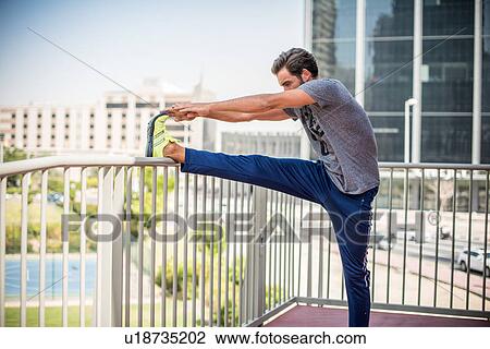 Stock Image - Man training, touching toes on balcony, Dubai, United Arab Emirates. Fotosearch