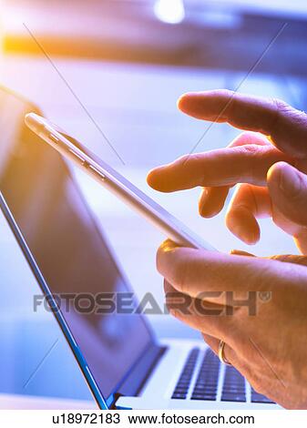 Stock Image - Man using a mobile phone with a laptop in the background. Fotosearch