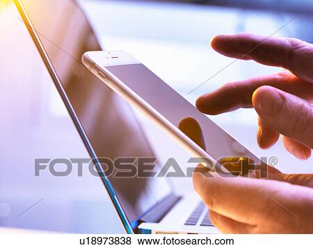 Man using a mobile phone with a laptop in the background View Large Photo Image Stock Photo - Man using a mobile phone with a laptop in the background. Fotosearch