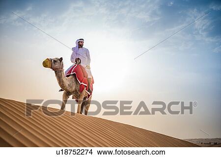 Man wearing traditional middle eastern clothes riding camel in desert, Dubai, United Arab Emirates View Large Photo Image Picture - Man wearing traditional middle eastern clothes riding camel in desert, Dubai, United Arab Emirates. Fotosearch