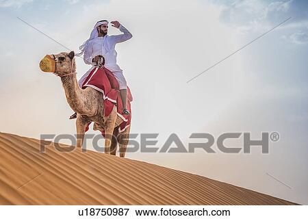 Man wearing traditional middle eastern clothes riding camel in desert, Dubai, United Arab Emirates View Large Photo Image Stock Photo - Man wearing traditional middle eastern clothes riding camel in desert, Dubai, United Arab Emirates. Fotosearch