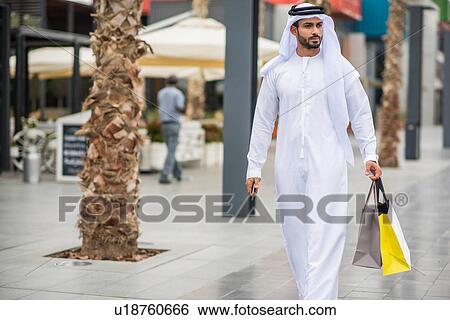 Man wearing traditional middle eastern clothing walking along street carrying shopping bags, Dubai, United Arab Emirates View Large Photo Image Stock Photograph - Man wearing traditional middle eastern clothing walking along street carrying shopping bags, Dubai, United Arab Emirates. Fotosearch