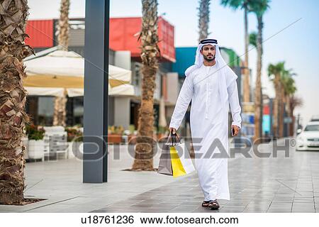 Man wearing traditional middle eastern clothing walking along street carrying shopping bags, Dubai, United Arab Emirates View Large Photo Image Stock Photograph - Man wearing traditional middle eastern clothing walking along street carrying shopping bags, Dubai, United Arab Emirates. Fotosearch