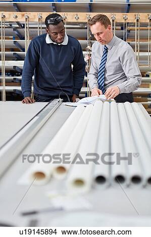 Picture - Manager and factory worker checking paperwork in roller blind factory. Fotosearch