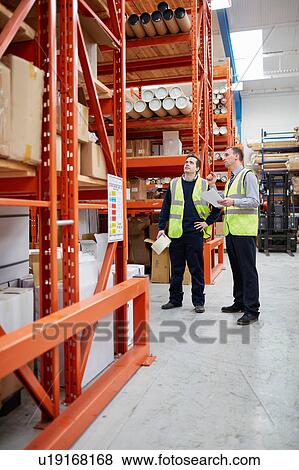Manager and male factory worker checking paperwork in factory warehouse View Large Photo Image Stock Photo - Manager and male factory worker checking paperwork in factory warehouse. Fotosearch