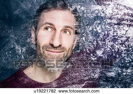 Stock Image - Mature bearded man looking through frosted window. Fotosearch