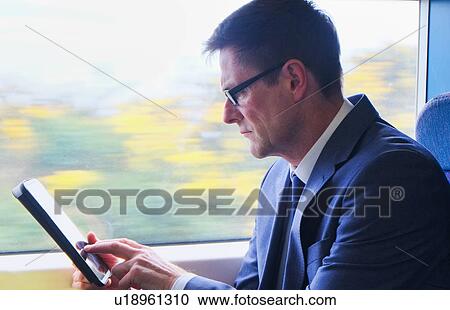 Stock Image - Mature businessman sitting on train, using digital tablet. Fotosearch