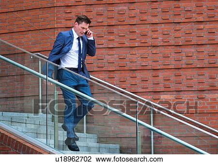 Stock Image - Mature businessman walking down steps, using smartphone. Fotosearch