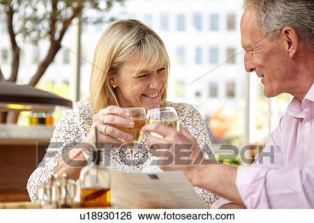Stock Photograph - Mature dating couple raising a glass of white wine at restaurant table. Fotosearch
