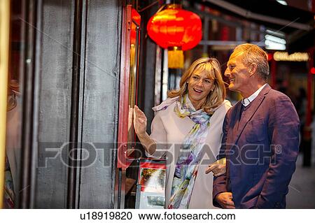 Stock Image - Mature dating couple reading restaurant menu in China Town, London, UK. Fotosearch
