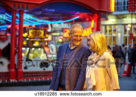 Stock Photography - Mature dating couple strolling on city street at night, London, UK. Fotosearch