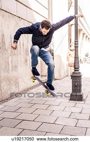 Stock Image - Mature man doing mid air skateboarding trick on city sidewalk. Fotosearch