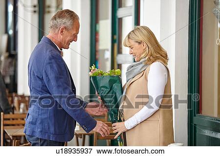 Stock Photo - Mature man handing date bouquet at sidewalk cafe table. Fotosearch