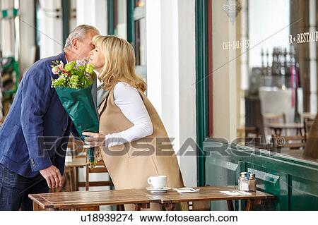 Picture - Mature man kissing date on cheek at sidewalk cafe table. Fotosearch