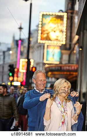 Stock Image - Mature man putting jacket over girlfriends shoulders on city street at dusk, London, UK. Fotosearch