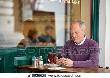 Mature man reading smartphone text at sidewalk cafe table View Large Photo Image Stock Photo - Mature man reading smartphone text at sidewalk cafe table. Fotosearch