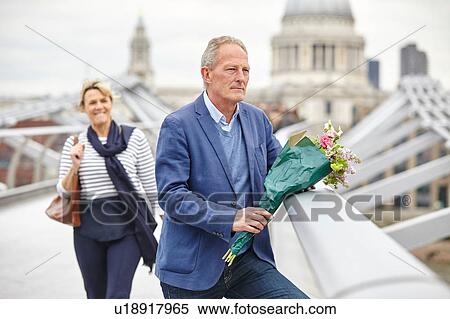Stock Photography - Mature man with bouquet waiting in front of date on Millennium Bridge, London, UK. Fotosearch