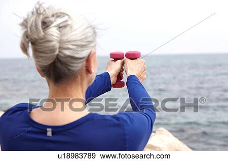 Mature woman beside sea, exercising with hand weights, rear view View Large Photo Image Stock Photo - Mature woman beside sea, exercising with hand weights, rear view. Fotosearch