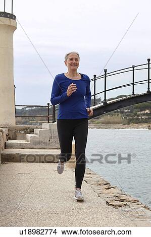 Picture - Mature woman exercising, running, outdoors. Fotosearch