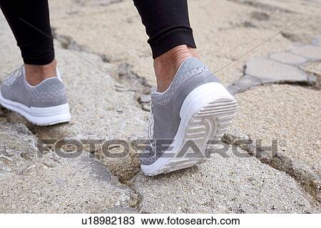 Stock Image - Mature woman exercising, running, outdoors, focus con feet. Fotosearch