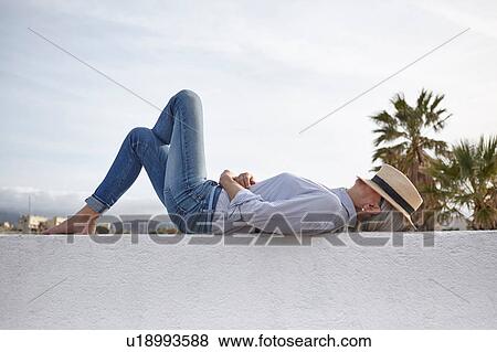 Stock Photo - Mature woman lying on wall, hat covering face. Fotosearch