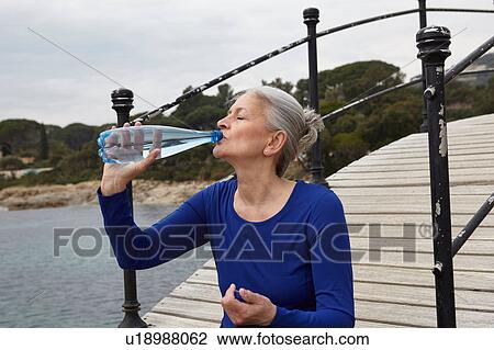 Stock Image - Mature woman outdoors, drinking from water bottle. Fotosearch