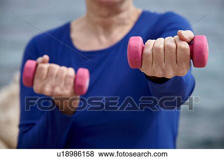 Stock Photo - Mature woman outdoors, exercising with hand weights. Fotosearch