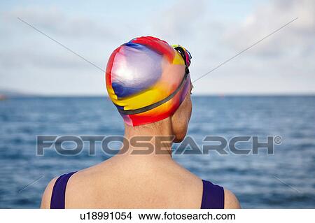Mature woman wearing swimming costume and swimming hat, standing beside the sea, rear view View Large Photo Image Picture - Mature woman wearing swimming costume and swimming hat, standing beside the sea, rear view. Fotosearch