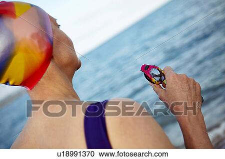 Mature woman wearing swimming costume, swimming hat and holding swimming goggles, standing beside the sea, rear view View Large Photo Image Stock Image - Mature woman wearing swimming costume, swimming hat and holding swimming goggles, standing beside the sea, rear view. Fotosearch