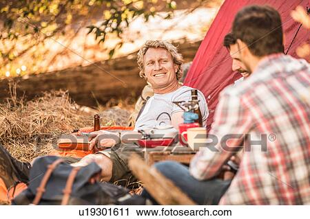 Stock Image - Men camping in forest drinking beer and coffee, Deer Park, Cape Town, South Africa. Fotosearch
