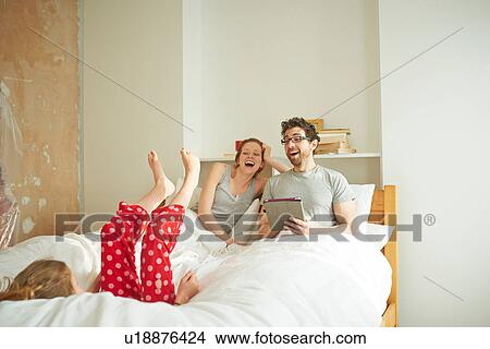 Picture - Mid adult couple having lie in whilst daughter falls back on bed. Fotosearch
