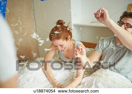 Picture - Mid adult couple having pillow fight with daughter in bed. Fotosearch