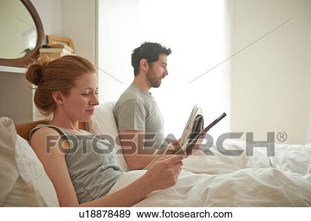 Mid adult couple reading digital tablet and broadsheet in bed View Large Photo Image Stock Photo - Mid adult couple reading digital tablet and broadsheet in bed. Fotosearch