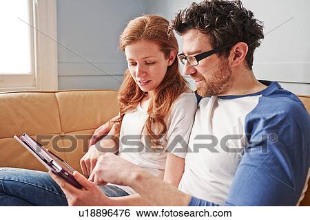 Stock Photograph - Mid adult couple relaxing on sofa looking at digital tablet. Fotosearch