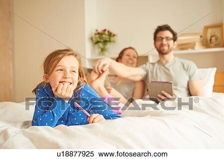 Stock Photography - Mid adult couple tickling daughters bare feet whilst having lie in. Fotosearch