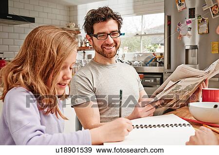 Mid adult man at breakfast table whilst daughter does homework View Large Photo Image Stock Photo - Mid adult man at breakfast table whilst daughter does homework. Fotosearch