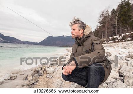 Mid adult man crouching beside lake, German Alps, Germany View Large Photo Image Stock Photography - Mid adult man crouching beside lake, German Alps, Germany. Fotosearch
