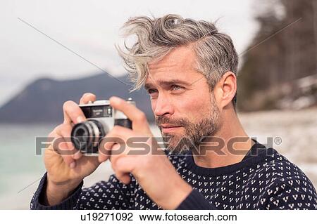 Stock Image - Mid adult man outdoors, holding camera, photographing scenery, German Alps, Germany. Fotosearch