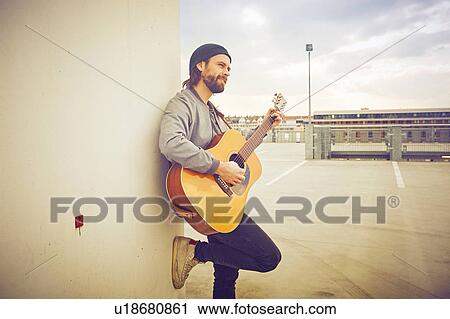 Mid adult man playing acoustic guitar on rooftop parking lot View Large Photo Image Stock Image - Mid adult man playing acoustic guitar on rooftop parking lot. Fotosearch