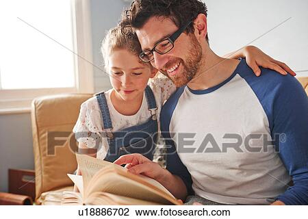 Mid adult man reading book with daughter on sofa View Large Photo Image Stock Image - Mid adult man reading book with daughter on sofa. Fotosearch
