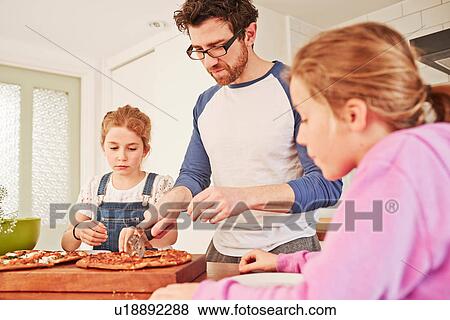 Mid adult man slicing pizza for daughters at kitchen bench View Large Photo Image Stock Photo - Mid adult man slicing pizza for daughters at kitchen bench. Fotosearch