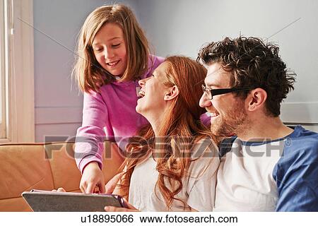 Stock Photograph - Mid adult parents and daughter on sofa looking at digital tablet. Fotosearch