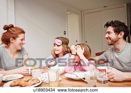 Picture - Mid adult parents at breakfast table with two daughters. Fotosearch