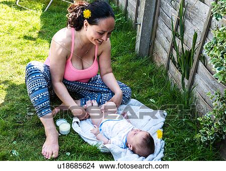 Mid adult woman changing baby son's nappy in garden View Large Photo Image Picture - Mid adult woman changing baby son's nappy in garden. Fotosearch