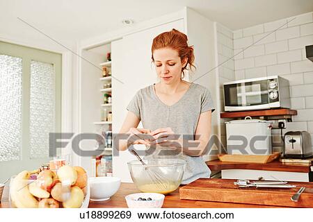 Stock Photo - Mid adult woman cracking eggs at kitchen counter. Fotosearch