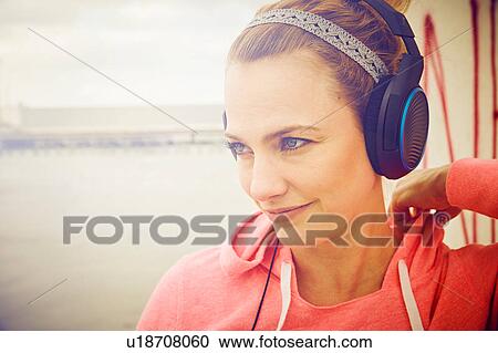 Stock Image - Mid adult woman listening to headphone music on rooftop parking lot. Fotosearch