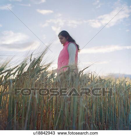 Stock Image - Mid adult woman, walking through wheat field. Fotosearch