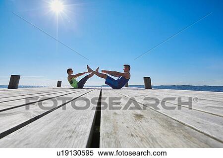 Stock Photography - Mid distance view of couple on pier face to face doing sit ups. Fotosearch