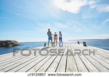 Stock Photo - Mid distance view of friends wearing sports clothes standing on pier. Fotosearch