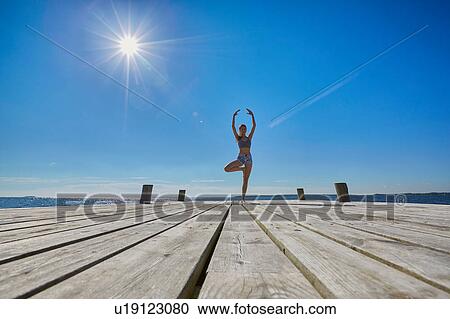 Mid distant view of woman on pier, standing on one leg arms raised View Large Photo Image Stock Image - Mid distant view of woman on pier, standing on one leg arms raised. Fotosearch